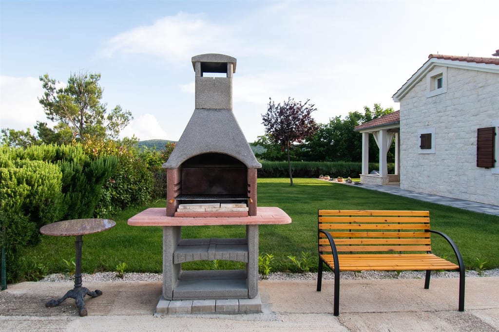 Stone barbecue and a bench at the edge of the lawn