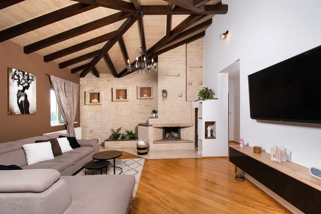 Living room with a beamed ceiling, a chandelier and a fireplace in a white stone wall