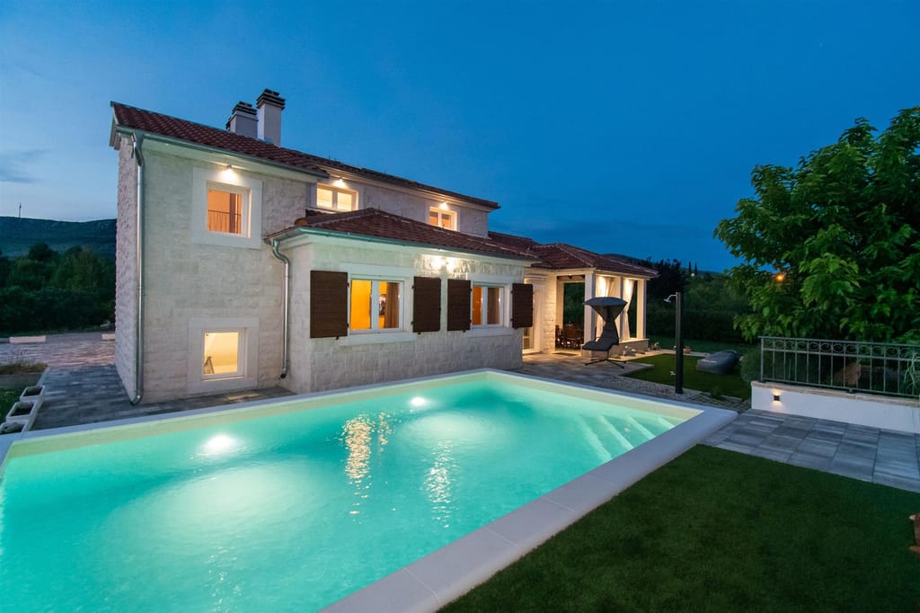 The villa lit up at night, seen from across the pool